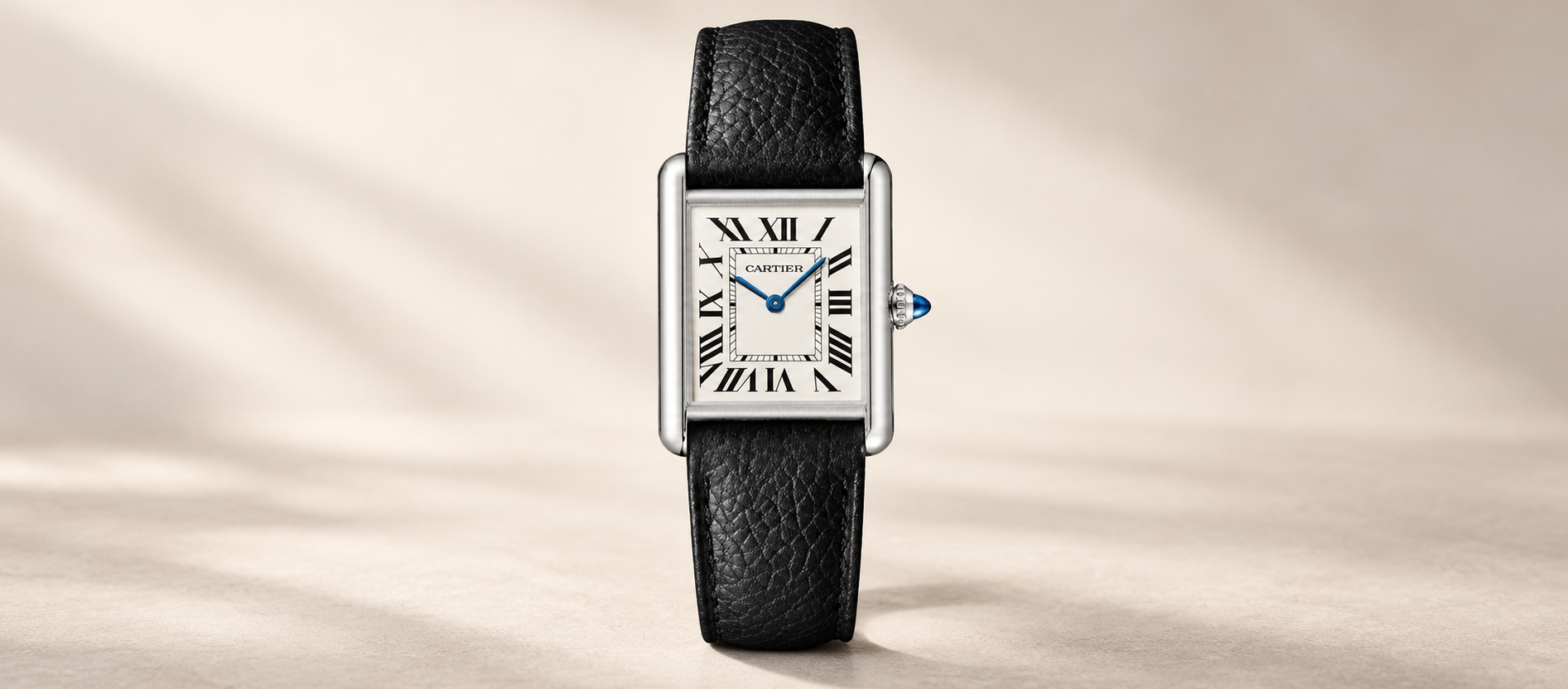 Cartier Tank Must Large WSTA0041 with a steel rectangular case, silvered Roman numeral dial and black leather strap against a warm neutral background.
