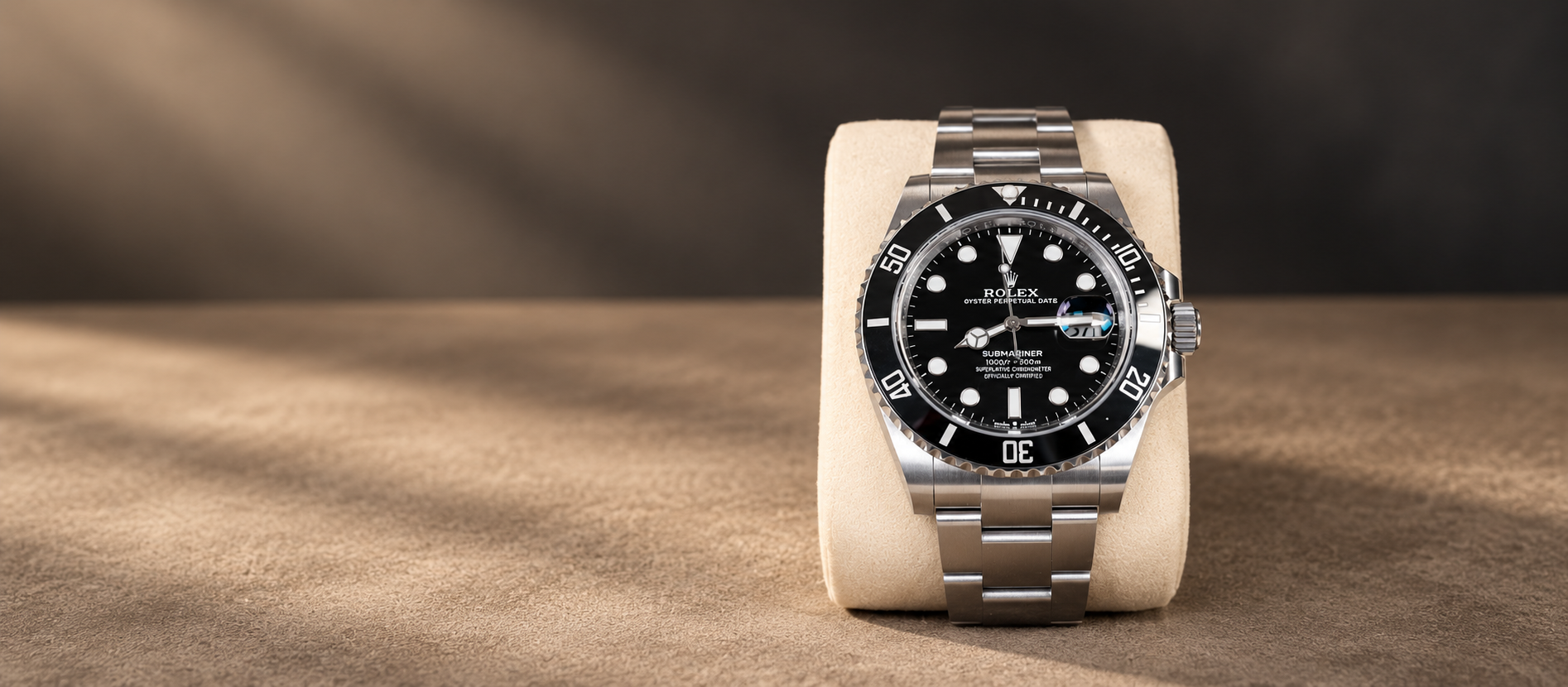 Rolex Submariner Date 126610LN with black dial, black bezel and steel Oyster bracelet on a cream cushion against a warm taupe background.