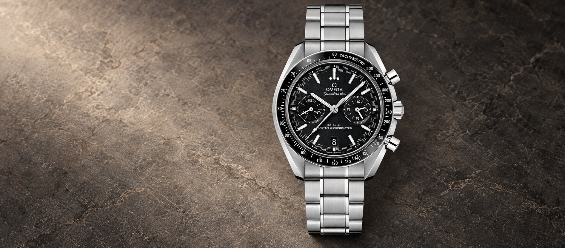 Omega Speedmaster Racing reference 329.30.44.51.01.001 with black two-counter dial, date display and steel bracelet against a warm charcoal stone background.