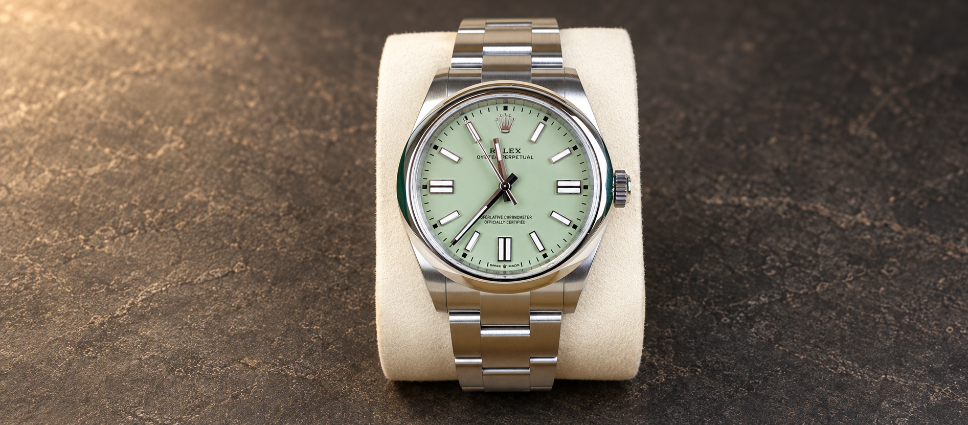 Rolex Oyster Perpetual 41 reference 134300 with pistachio dial and steel Oyster bracelet on a cream cushion against warm charcoal stone.